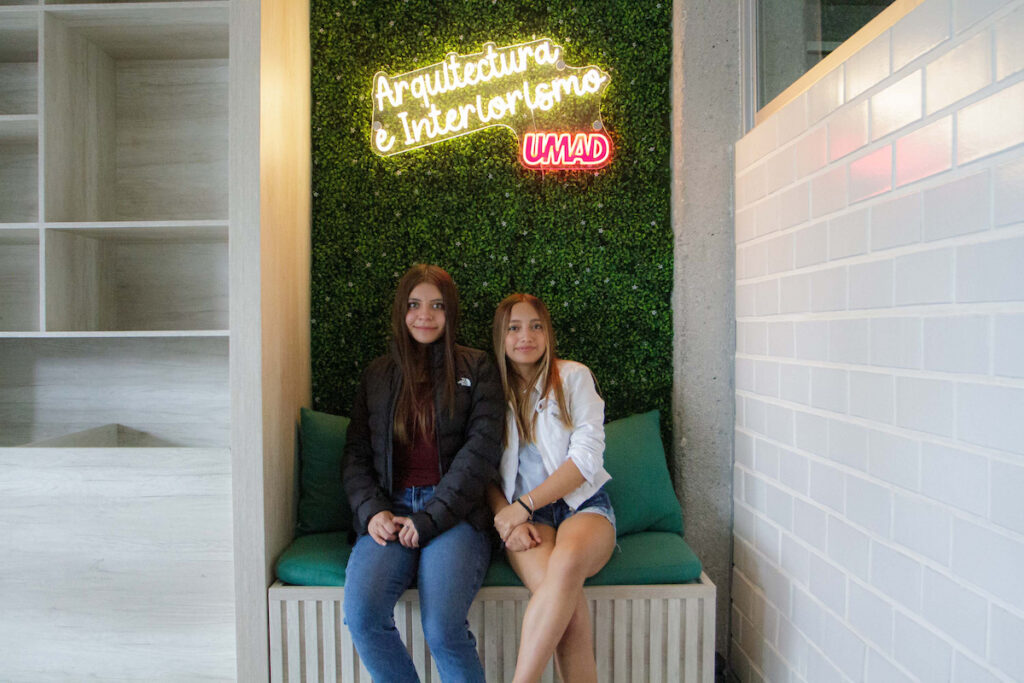 Dos estudiantes felices en el estudio de arquitectura UMAD, reflejo del bienestar y compañerismo.