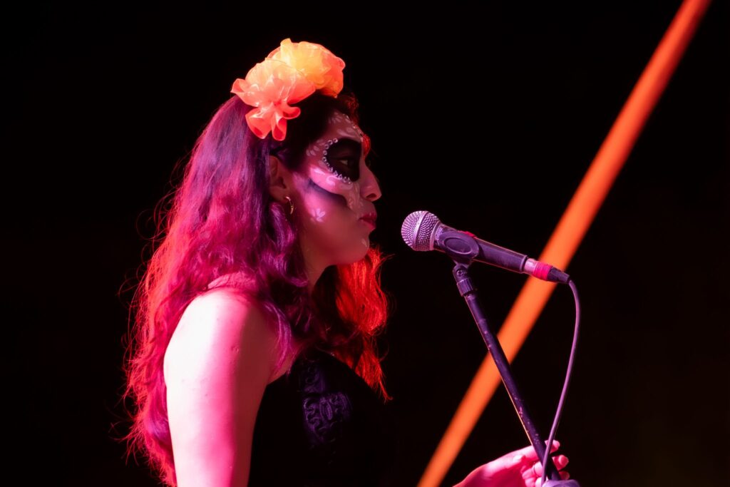 Evento cultural en la UMAD donde una estudiante canta caracterizada como catrina.