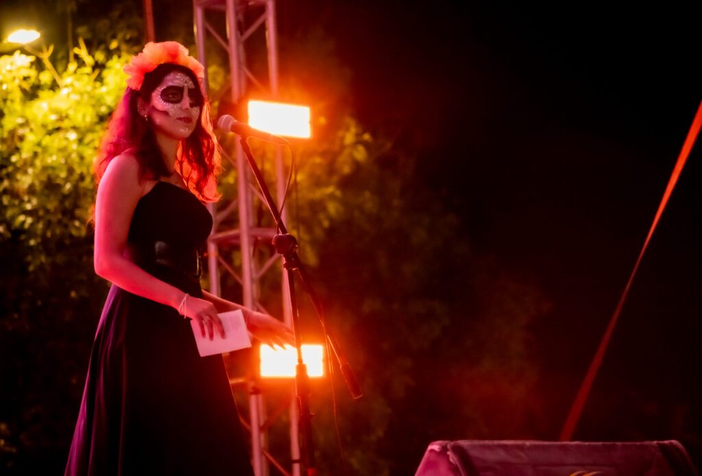 Estudiante UMAD caracterizada como catrina interpretando una canción durante un evento cultural.